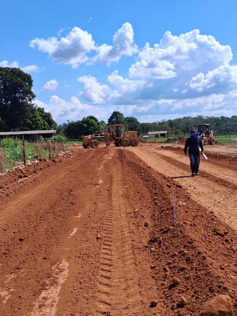Técnico da SV Topografia caminhando em via em construção com motoniveladora ao fundo