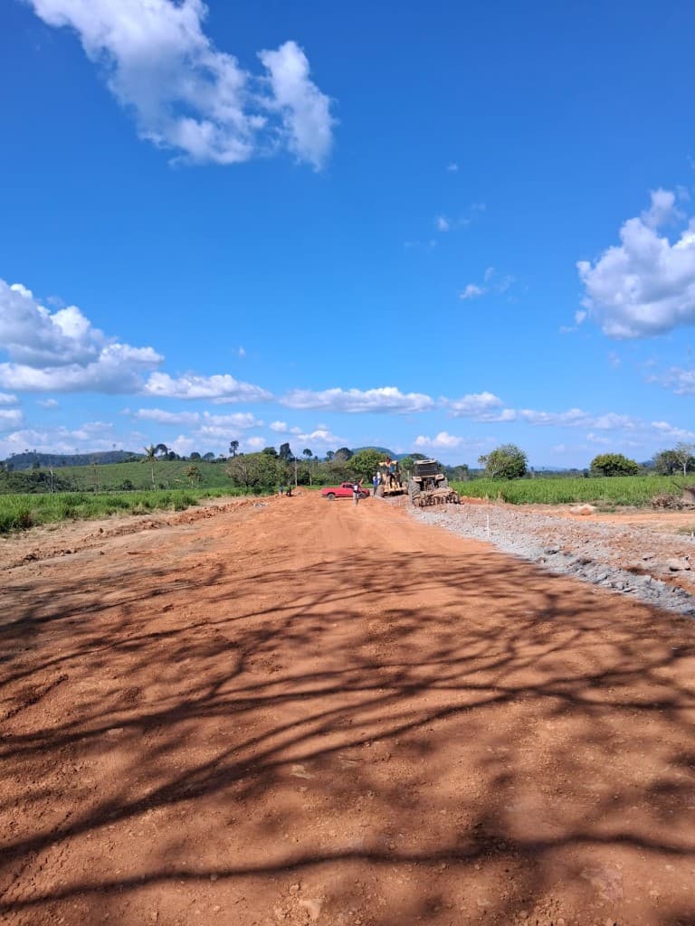 Vista ampla de obra de estrada com motoniveladora, trator e veículos de apoio
