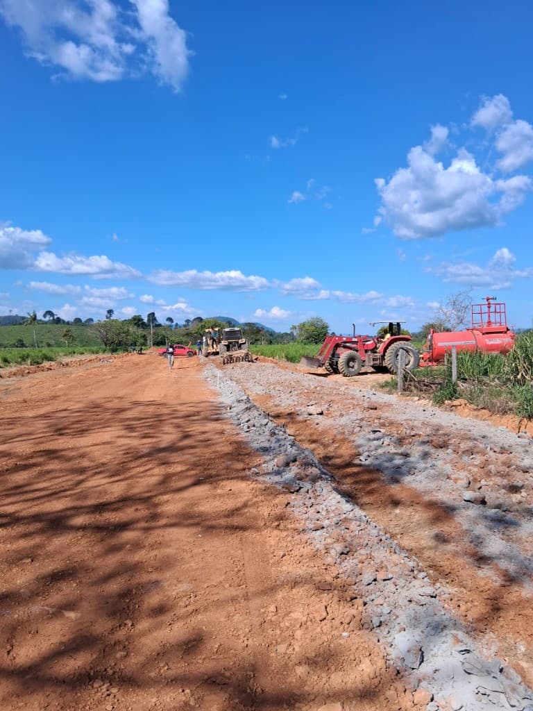 Trator com tanque de água aplicando base de brita em obra de abertura de via